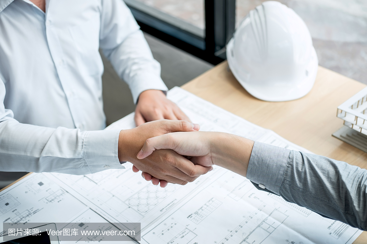 合作伙伴握手,建筑工程或建筑師討論藍圖和建筑模型,同時檢查草圖信息,為建筑項目的合作伙伴舉行會議